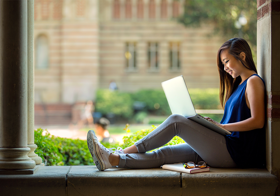 young woman outdoors in a college settings working on a laptop