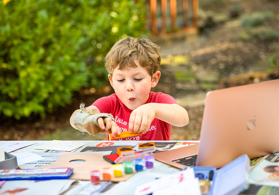 Child at a table outside doing crafts near an open laptop